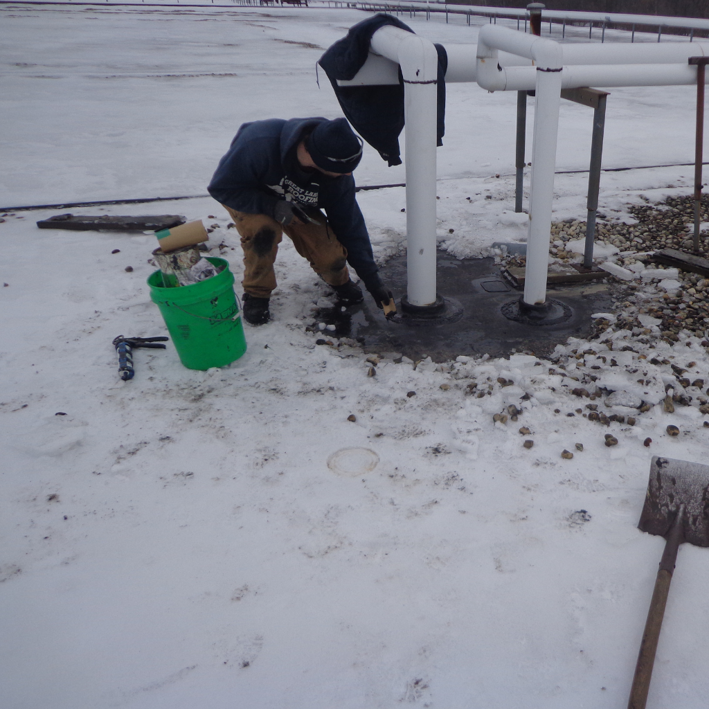 Part of a 2-person repair team works to identify and mend a leak on a snowy rooftop
